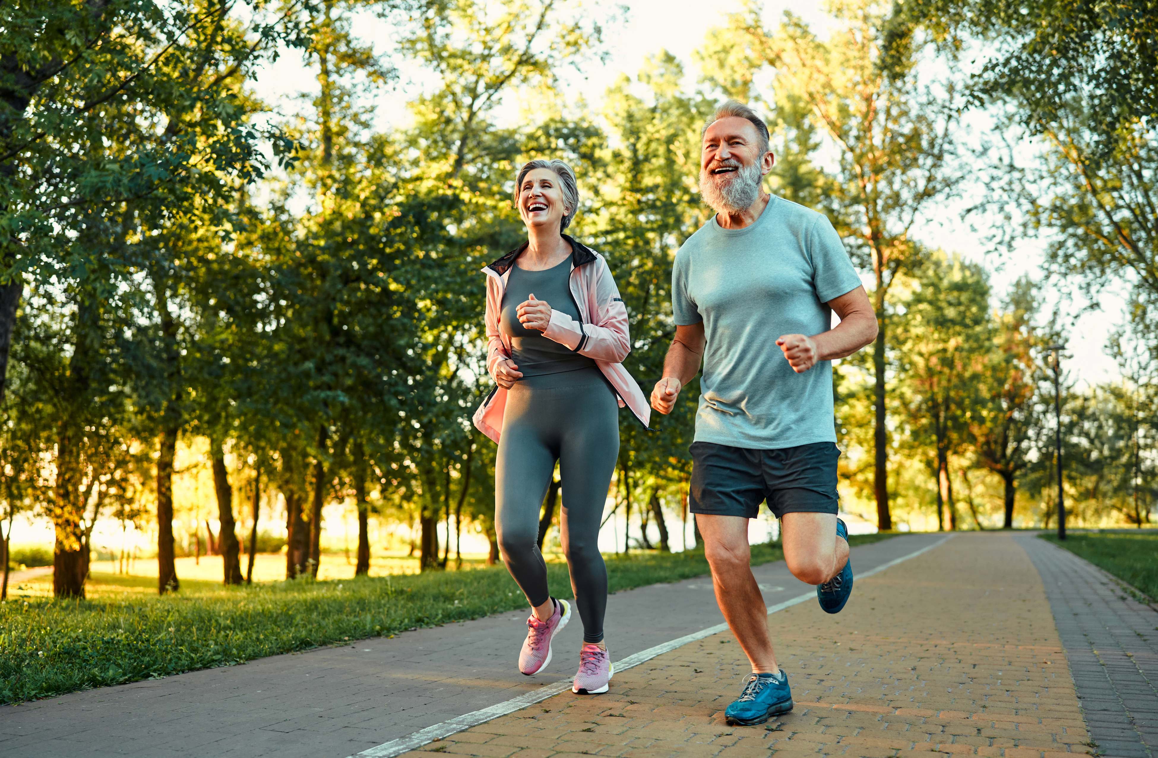 Smiling active couple jogging together on a sunlit park path
