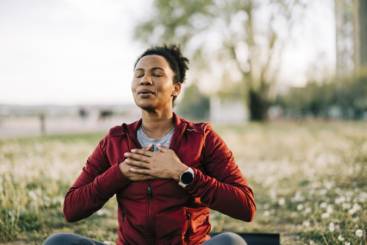 Woman sitting outdoors with eyes closed and hands on her chest, breathing calmly