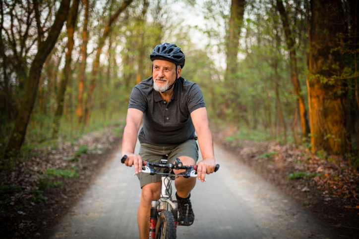 Active older man wearing a helmet riding a bike along a tree-lined trail